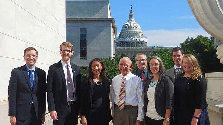 group poses for photo in business attire with capitol building in background